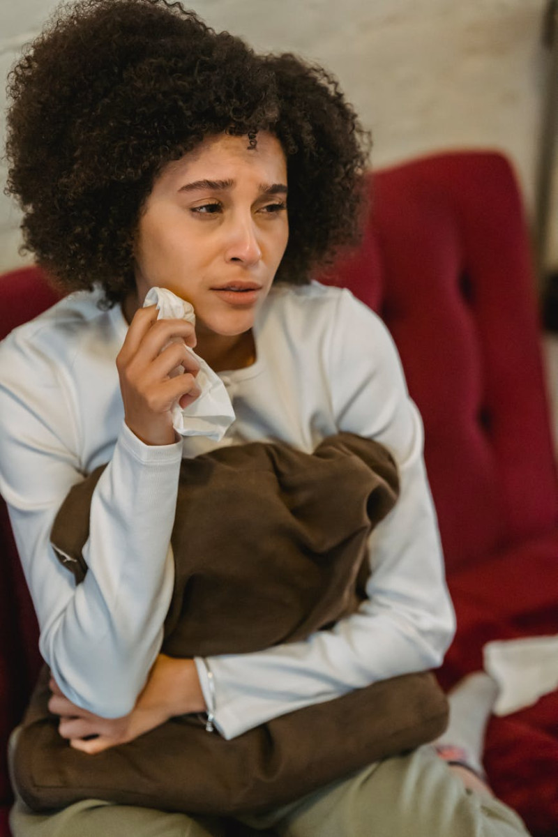 depressed young ethnic female embracing pillow and crying sitting on cozy sofa